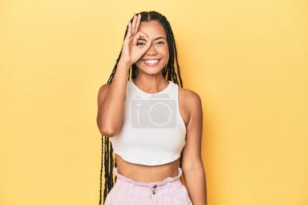 Foto de Joven mujer indonesia en amarillo estudio telón de fondo emocionado mantener el gesto bien en el ojo. - Imagen libre de derechos