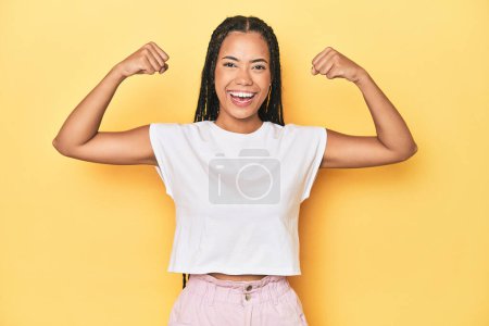 Photo for Young Indonesian woman on yellow studio backdrop showing strength gesture with arms, symbol of feminine power - Royalty Free Image
