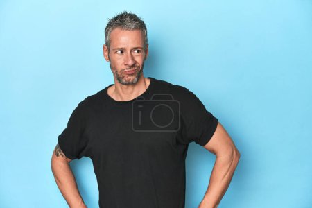 Photo for Middle-aged caucasian man on blue backdrop confused, feels doubtful and unsure. - Royalty Free Image