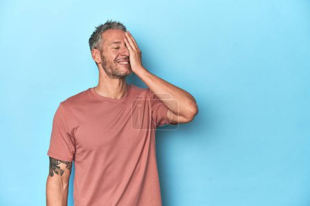Photo for Middle-aged caucasian man on blue backdrop laughing happy, carefree, natural emotion. - Royalty Free Image