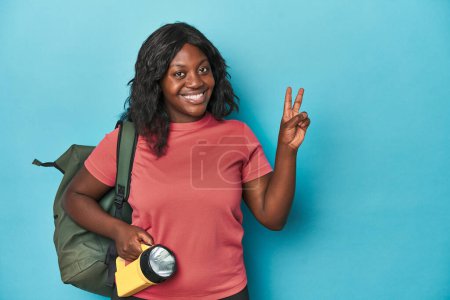 Photo for Curvy explorer with backpack and flashlight joyful and carefree showing a peace symbol with fingers. - Royalty Free Image