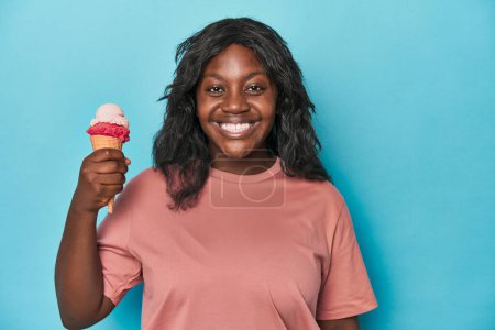 Photo for Young curvy woman enjoying ice-cream on a blue backdrop - Royalty Free Image