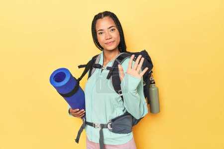 Téléchargez les photos : Femme indonésienne prête pour le voyage en montagne sur jaune souriant gai montrant numéro cinq avec les doigts. - en image libre de droit