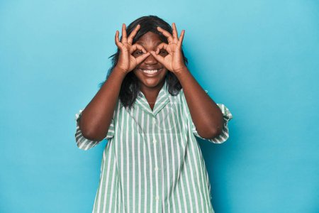 Téléchargez les photos : Jeune femme courbée afro-américaine montrant un signe acceptable sur les yeux - en image libre de droit