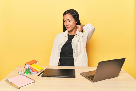 Téléchargez les photos : Designer indonésien avec des outils à table sur le dos jaune toucher de la tête, penser et faire un choix. - en image libre de droit