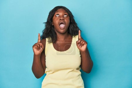 Téléchargez les photos : Jeune femme afro-américaine courbée pointant à l'envers avec la bouche ouverte. - en image libre de droit