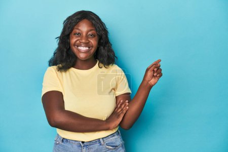 Téléchargez les photos : Jeune femme afro-américaine courbée souriante pointant joyeusement avec l'index loin. - en image libre de droit
