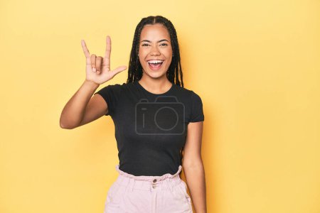 Photo for Young Indonesian woman on yellow studio backdrop showing a horns gesture as a revolution concept. - Royalty Free Image