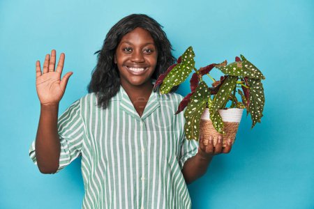 Téléchargez les photos : Curvy jardinier tenant plante en studio souriant gai montrant numéro cinq avec les doigts. - en image libre de droit