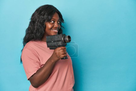 Téléchargez les photos : Femme courbée avec une caméra de cinéma vintage sur fond bleu - en image libre de droit