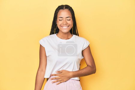Photo for Young Indonesian woman on yellow studio backdrop touches tummy, smiles gently, eating and satisfaction concept. - Royalty Free Image
