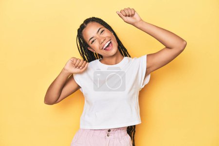 Photo for Young Indonesian woman on yellow studio backdrop celebrating a special day, jumps and raise arms with energy. - Royalty Free Image