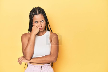 Téléchargez les photos : Jeune femme indonésienne sur fond de studio jaune qui se sent triste et coûteuse, regardant l'espace de copie. - en image libre de droit