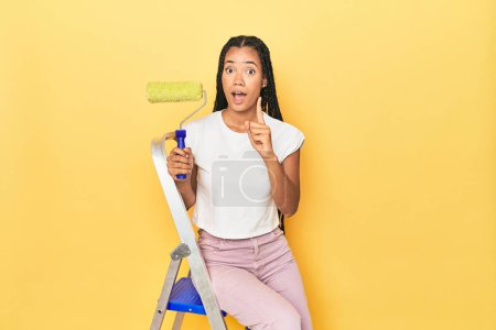 Photo for Indonesian woman with roller on ladder on yellow having an idea, inspiration concept. - Royalty Free Image