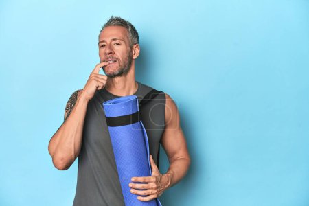 Photo for Athlete with a mat on a blue studio backdrop relaxed thinking about something looking at a copy space. - Royalty Free Image