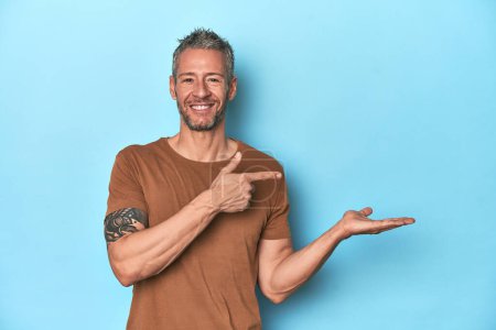 Photo for Middle-aged caucasian man on blue backdrop excited holding a copy space on palm. - Royalty Free Image