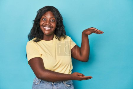 Téléchargez les photos : Jeune femme afro-américaine courbée choquée et étonnée tenant un espace de copie entre les mains. - en image libre de droit