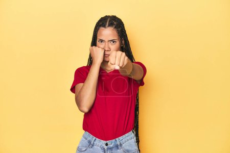 Photo for Young Indonesian woman on yellow studio backdrop throwing a punch, anger, fighting due to an argument, boxing. - Royalty Free Image