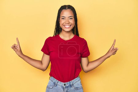 Photo for Young Indonesian woman on yellow studio backdrop indicates with both fore fingers up showing a blank space. - Royalty Free Image