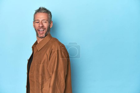 Foto de Hombre caucásico de mediana edad sobre fondo azul mira a un lado sonriente, alegre y agradable. - Imagen libre de derechos