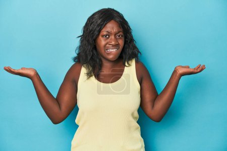 Téléchargez les photos : Jeune femme afro-américaine courbée confuse et douteuse haussant les épaules pour tenir un espace de copie. - en image libre de droit