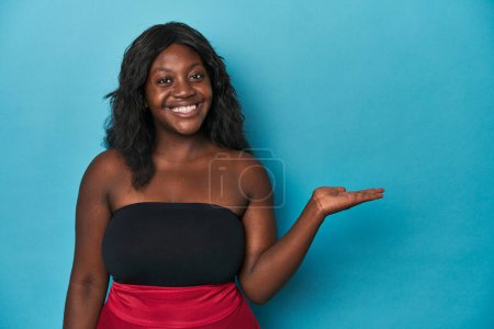 Téléchargez les photos : Jeune femme afro-américaine courbée montrant un espace de copie sur une paume et tenant une autre main à la taille. - en image libre de droit