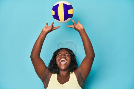 Téléchargez les photos : Femme courbée sportive pratiquant le volley-ball sert sur fond bleu - en image libre de droit