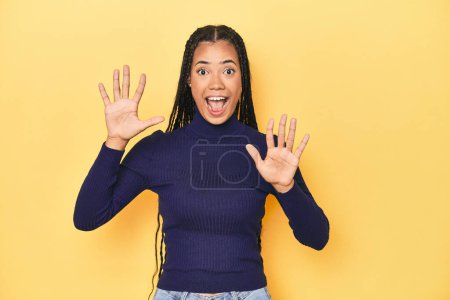 Téléchargez les photos : Jeune femme indonésienne sur fond de studio jaune recevant une agréable surprise, excitée et levant la main. - en image libre de droit
