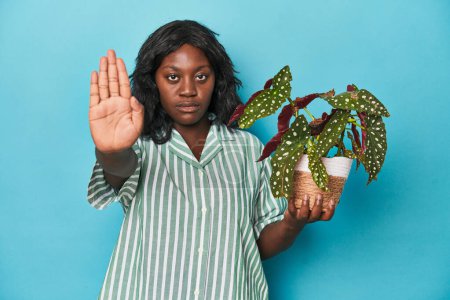 Photo for Curvy gardener holding plant in studio standing with outstretched hand showing stop sign, preventing you. - Royalty Free Image