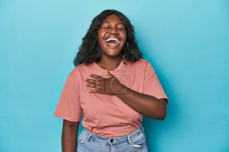 Foto de Joven africana americana curvilínea se ríe en voz alta manteniendo la mano en el pecho. - Imagen libre de derechos