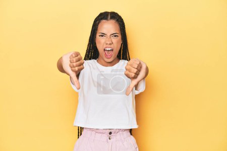 Photo for Young Indonesian woman on yellow studio backdrop showing thumb down and expressing dislike. - Royalty Free Image