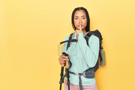 Photo for Indonesian woman with hiking gear on yellow keeping a secret or asking for silence. - Royalty Free Image