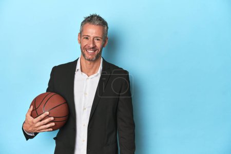 Téléchargez les photos : Coach de basket tenant une balle sur fond de studio bleu - en image libre de droit