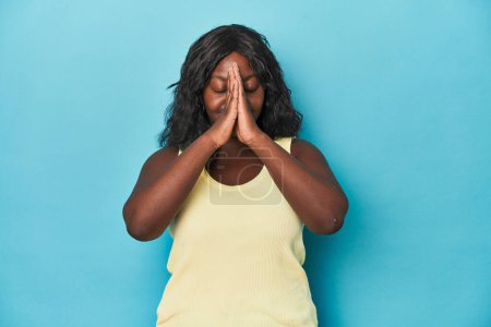 Téléchargez les photos : Jeune femme courbée afro-américaine tenant la main dans la prière près de la bouche, se sent confiant. - en image libre de droit