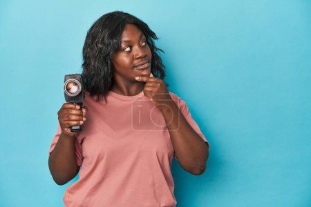Photo for Curvy lady with vintage film camera looking sideways with doubtful and skeptical expression. - Royalty Free Image