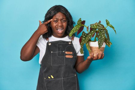 Photo for Curvy gardener holding plant in studio showing a disappointment gesture with forefinger. - Royalty Free Image