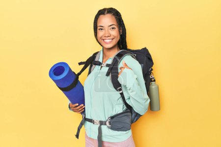 Téléchargez les photos : Femme indonésienne prête pour un voyage en montagne sur une personne jaune pointant à la main vers un espace de copie de chemise, fière et confiante - en image libre de droit