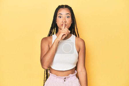Photo for Young Indonesian woman on yellow studio backdrop keeping a secret or asking for silence. - Royalty Free Image