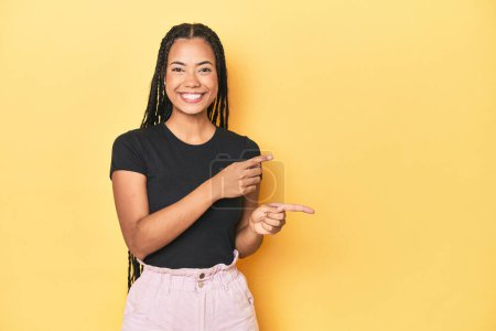 Photo for Young Indonesian woman on yellow studio backdrop excited pointing with forefingers away. - Royalty Free Image