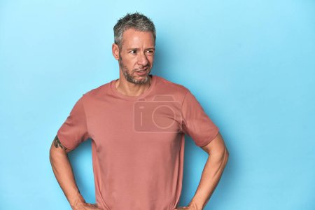 Photo for Middle-aged caucasian man on blue backdrop confused, feels doubtful and unsure. - Royalty Free Image