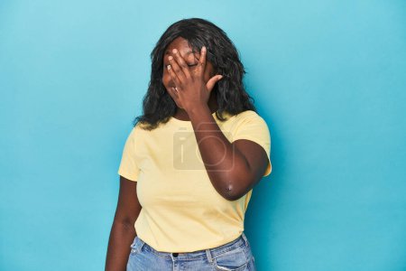 Téléchargez les photos : Jeune femme afro-américaine courbée cligner des yeux à la caméra par les doigts, embarrassé couvrant le visage. - en image libre de droit