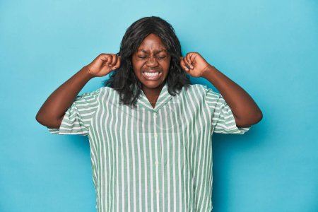 Foto de Joven africana americana curvilínea cubriendo las orejas con los dedos, estresada y desesperada por un ambiente ruidoso. - Imagen libre de derechos