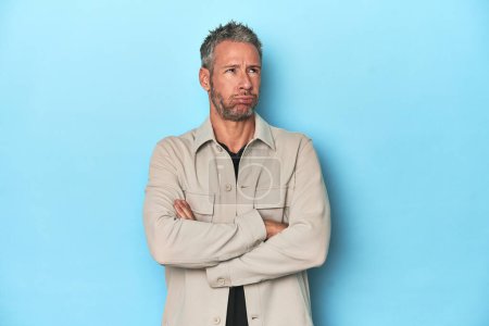 Photo for Middle-aged caucasian man on blue backdrop tired of a repetitive task. - Royalty Free Image