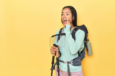 Photo for Indonesian woman with hiking gear on yellow shouting and holding palm near opened mouth. - Royalty Free Image
