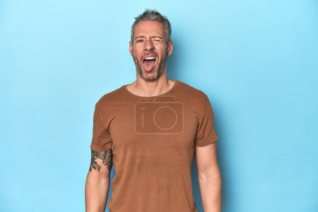 Foto de Hombre caucásico de mediana edad en telón de fondo azul divertida y amigable sobresaliendo lengua. - Imagen libre de derechos