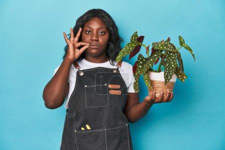 Téléchargez les photos : Jardinier courbé tenant plante en studio avec les doigts sur les lèvres gardant un secret. - en image libre de droit