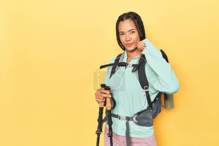 Téléchargez les photos : Femme indonésienne avec équipement de randonnée sur jaune se sent fier et confiant, exemple à suivre. - en image libre de droit