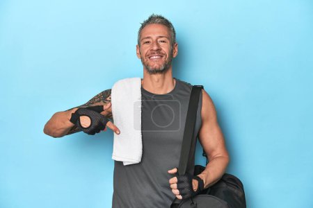 Photo for Athlete with gym backpack on blue background person pointing by hand to a shirt copy space, proud and confident - Royalty Free Image