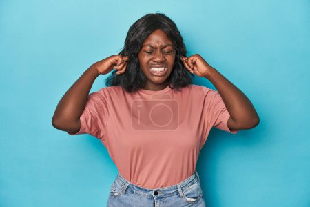 Téléchargez les photos : Jeune femme afro-américaine courbée couvrant les oreilles avec des doigts, stressée et désespérée par une ambiance bruyante. - en image libre de droit