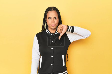 Photo for Indonesian woman in classic black baseball jacket showing a dislike gesture, thumbs down. Disagreement concept. - Royalty Free Image